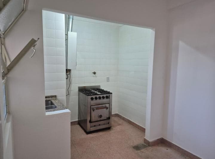 Cocina con anafe, horno, bacha, termotanque y azulejos blancos.