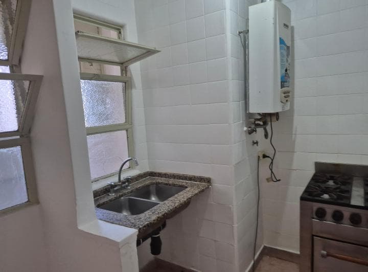 Cocina con bacha doble, grifería, termotanque y azulejos blancos.