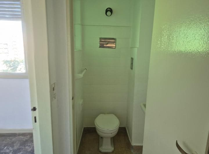 Toilette con inodoro y paredes de azulejos blancos.