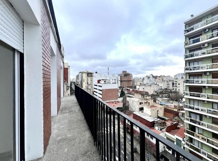 Balcón largo con vista a la ciudad, edificios altos y cielo nublado.