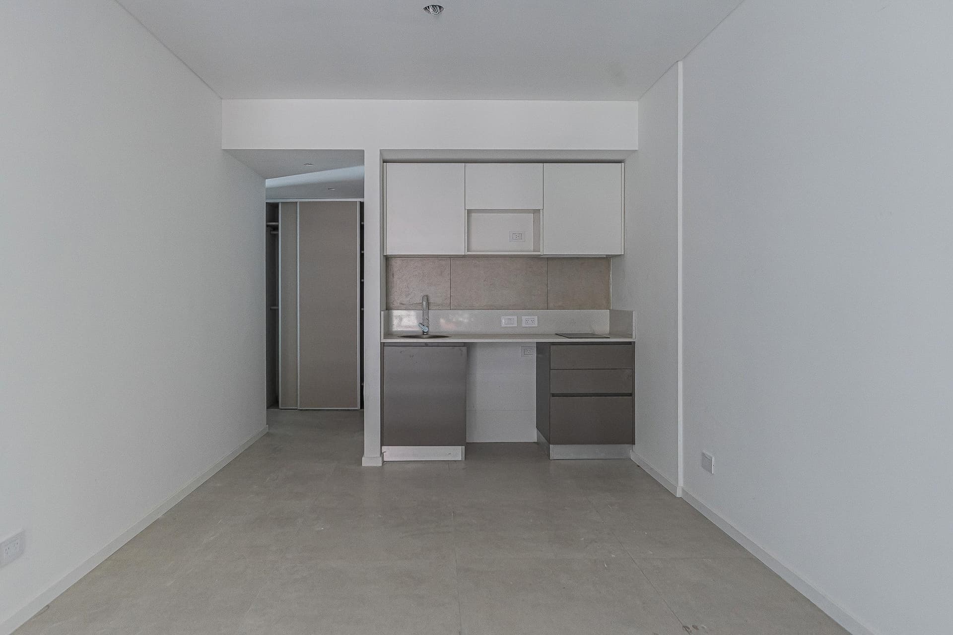 Cocina integrada con mesada, bacha y alacenas, vista desde el ambiente principal.