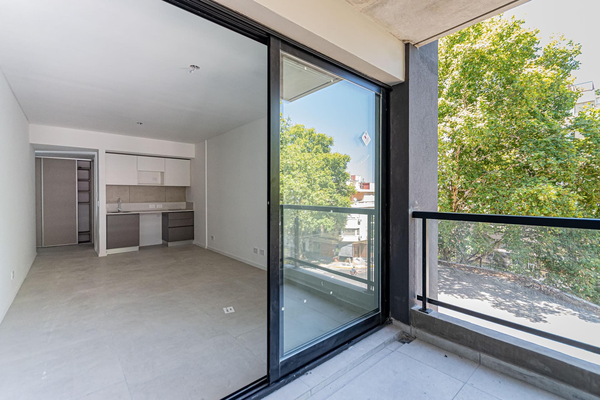 Balcón con puerta corrediza de vidrio y vista al interior con cocina.