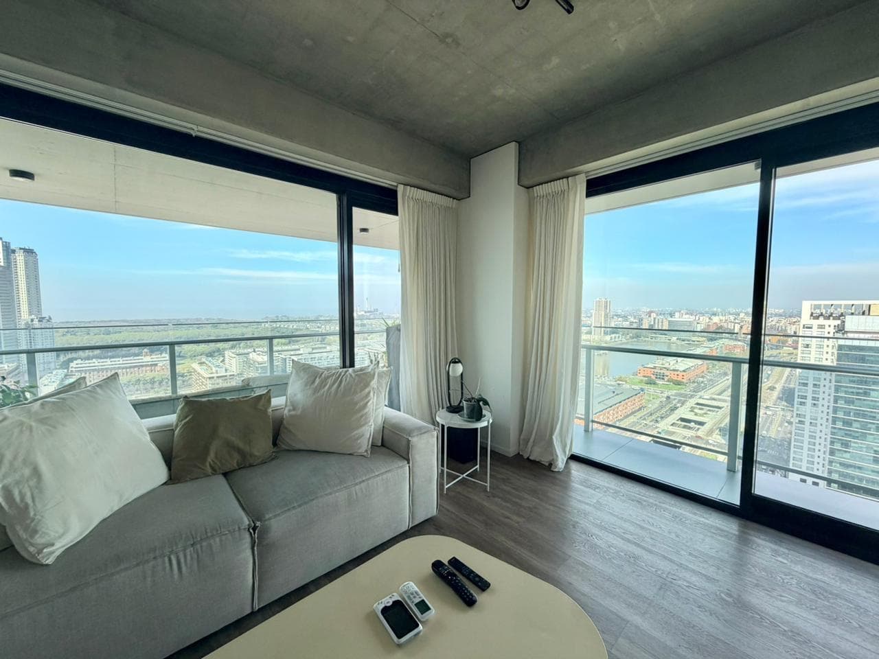 Living con sillón, ventanales y vista a la ciudad, techo de hormigón.