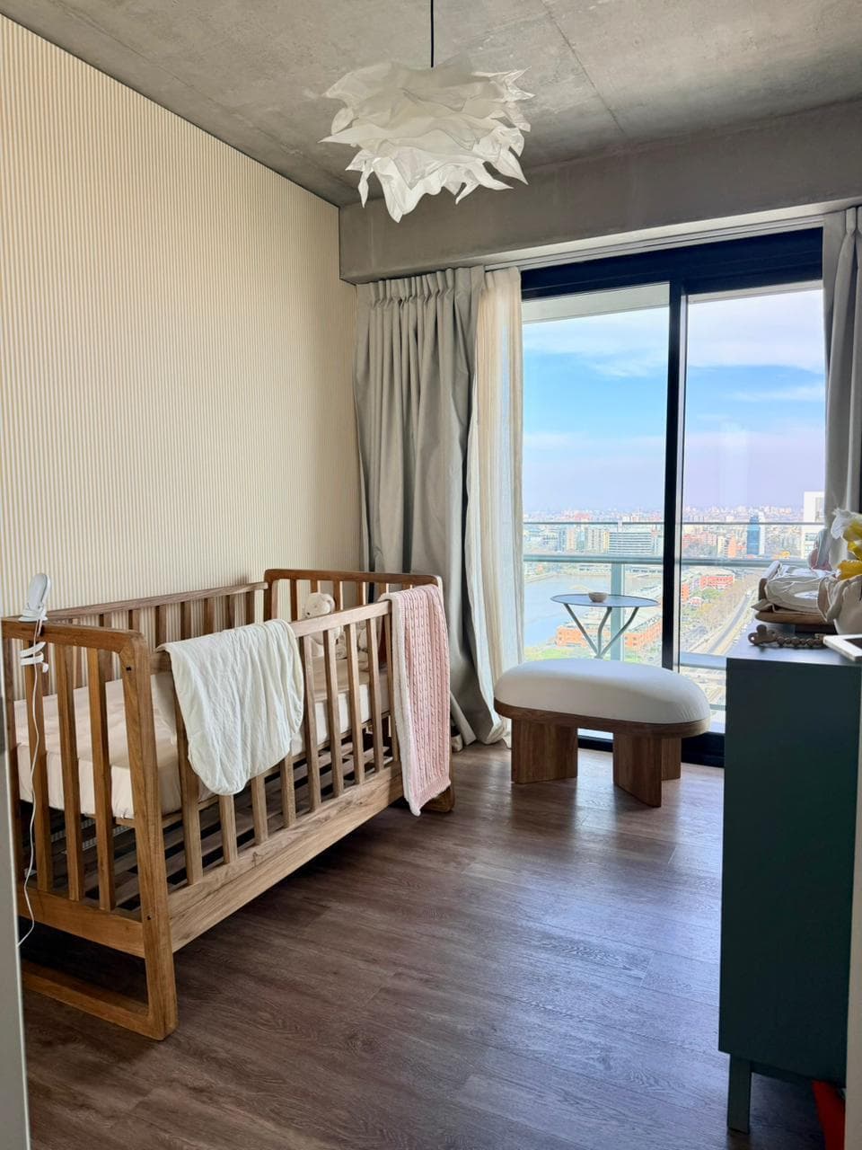Dormitorio de bebé con cuna de madera, cambiador y ventanal amplio.