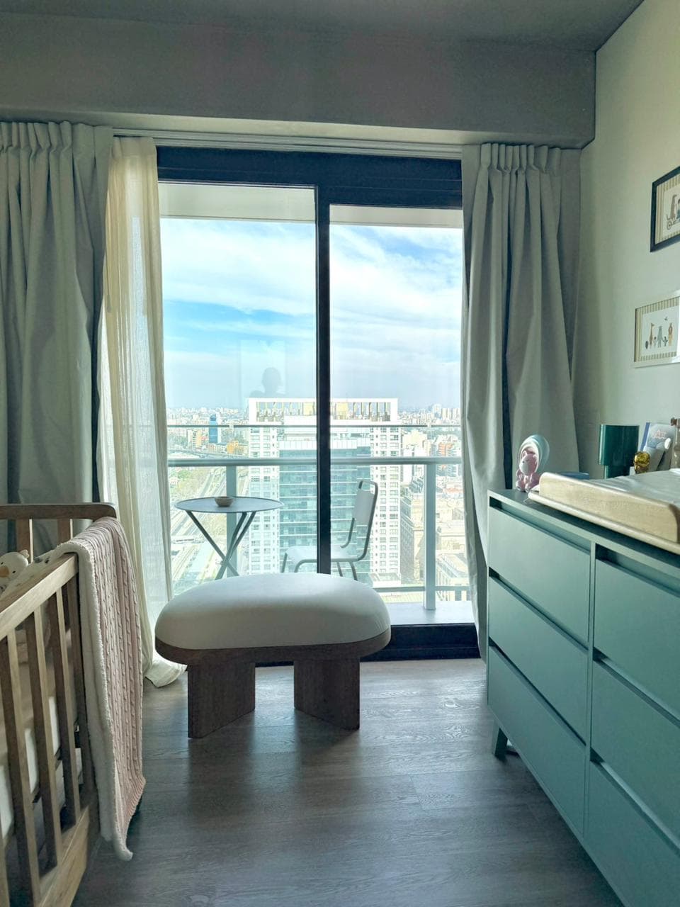 Dormitorio infantil con cuna, mueble cambiador y ventanal con vista exterior.