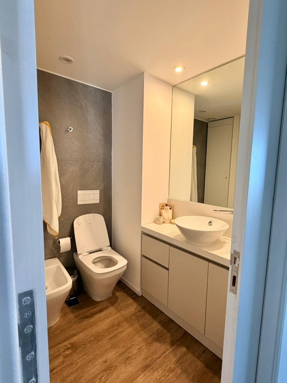 Baño con inodoro, bidet y vanitory, paredes grises y blancas.
