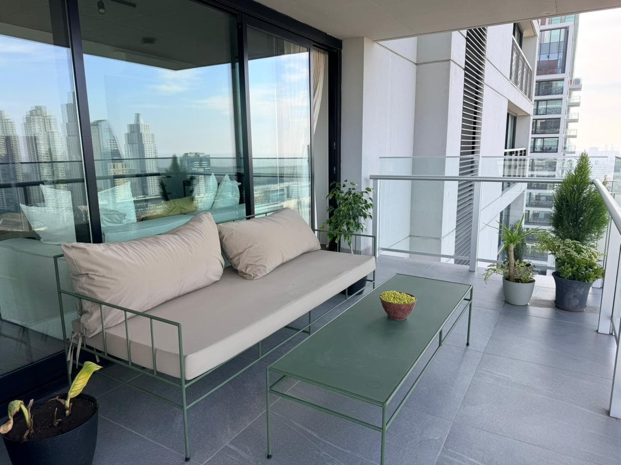 Balcón terraza con mobiliario de exterior, plantas y vista a edificios.