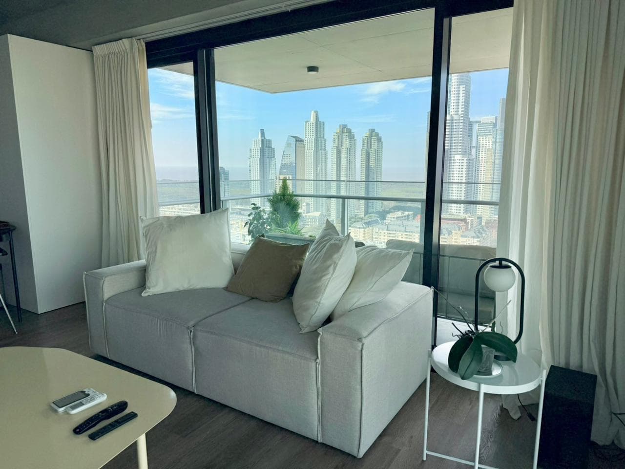 Living con sillón, mesa auxiliar y ventanal con vista panorámica a la ciudad.