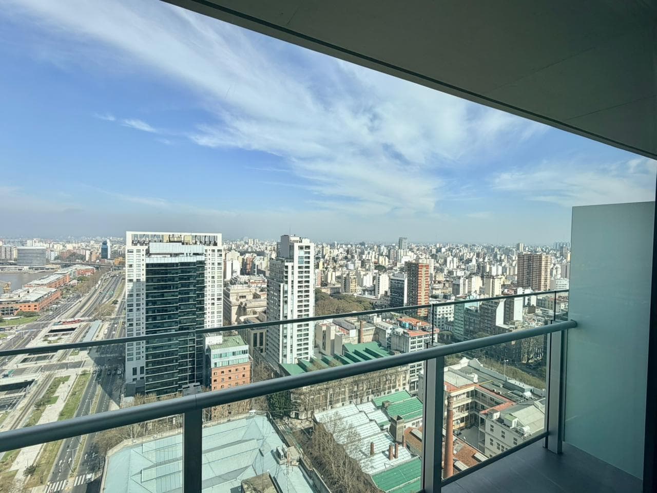 Vista desde balcón a la ciudad con edificios, río y cielo azul.