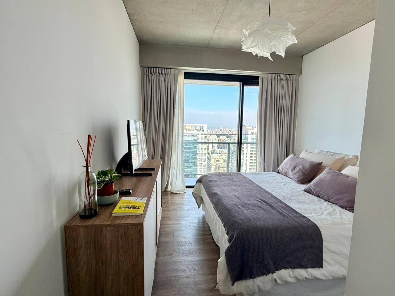 Dormitorio con cama, cómoda con TV y ventanal con vista.