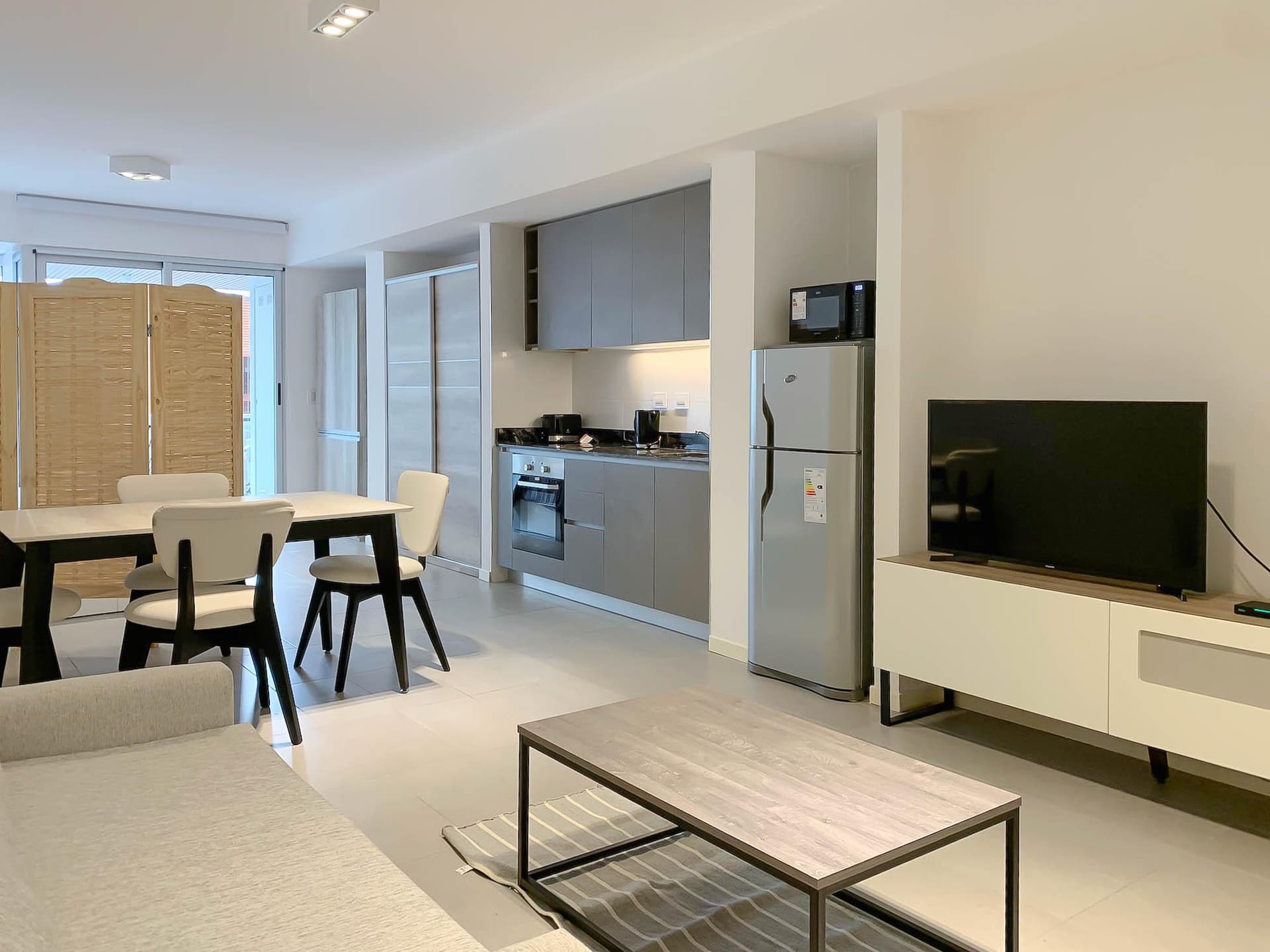 Living con sofá, mesa, cocina integrada y heladera, televisión.