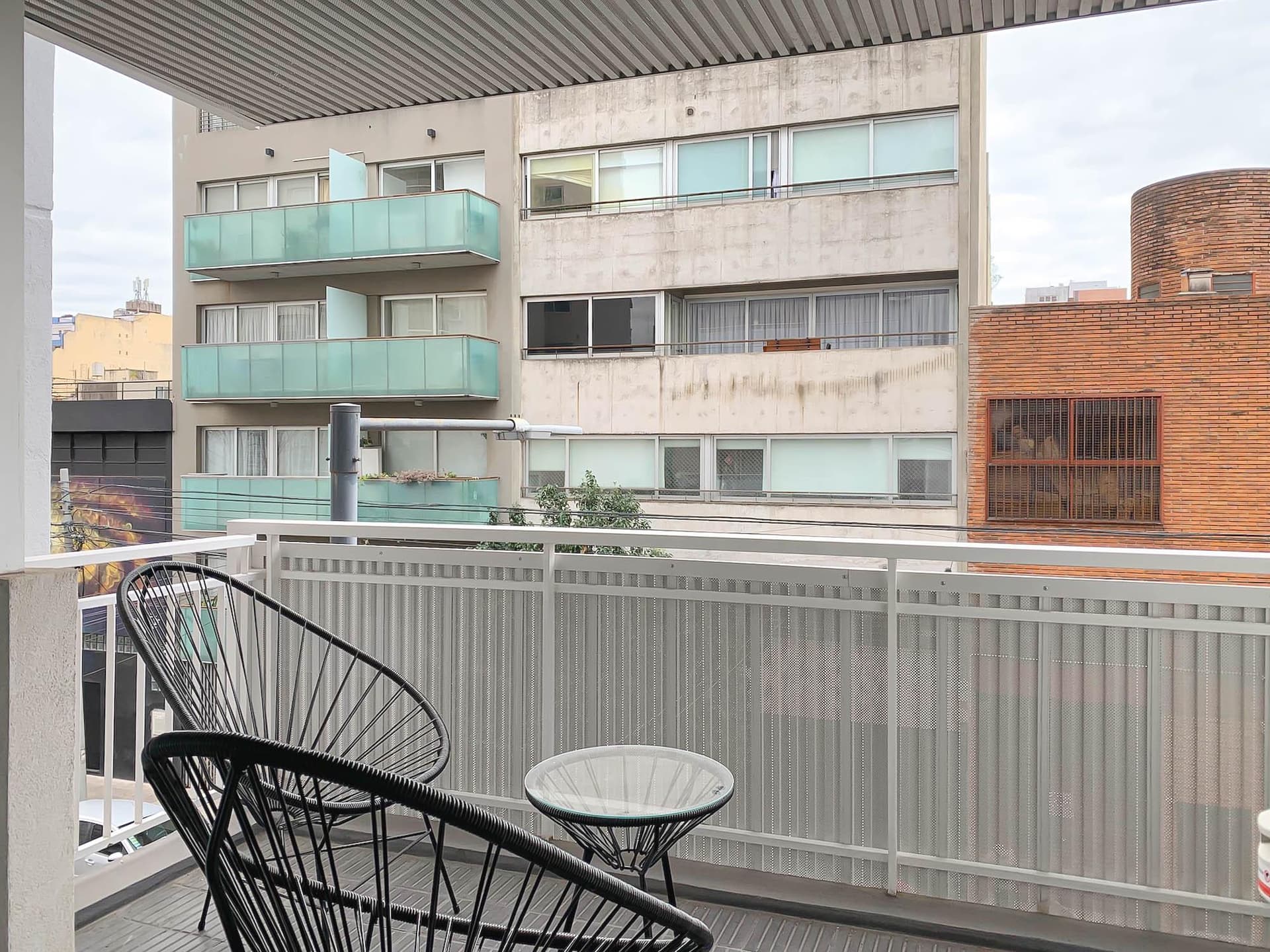 Balcón con silla Acapulco, mesa pequeña y vista a edificios.
