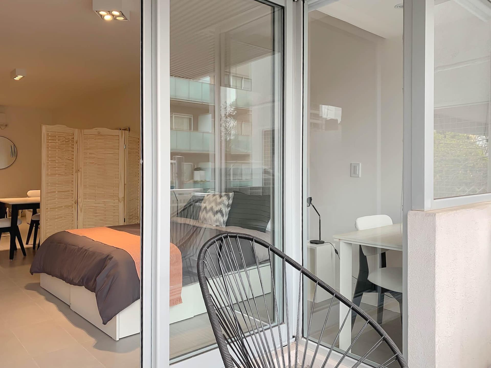 Balcón con silla Acapulco y puerta corrediza de vidrio.