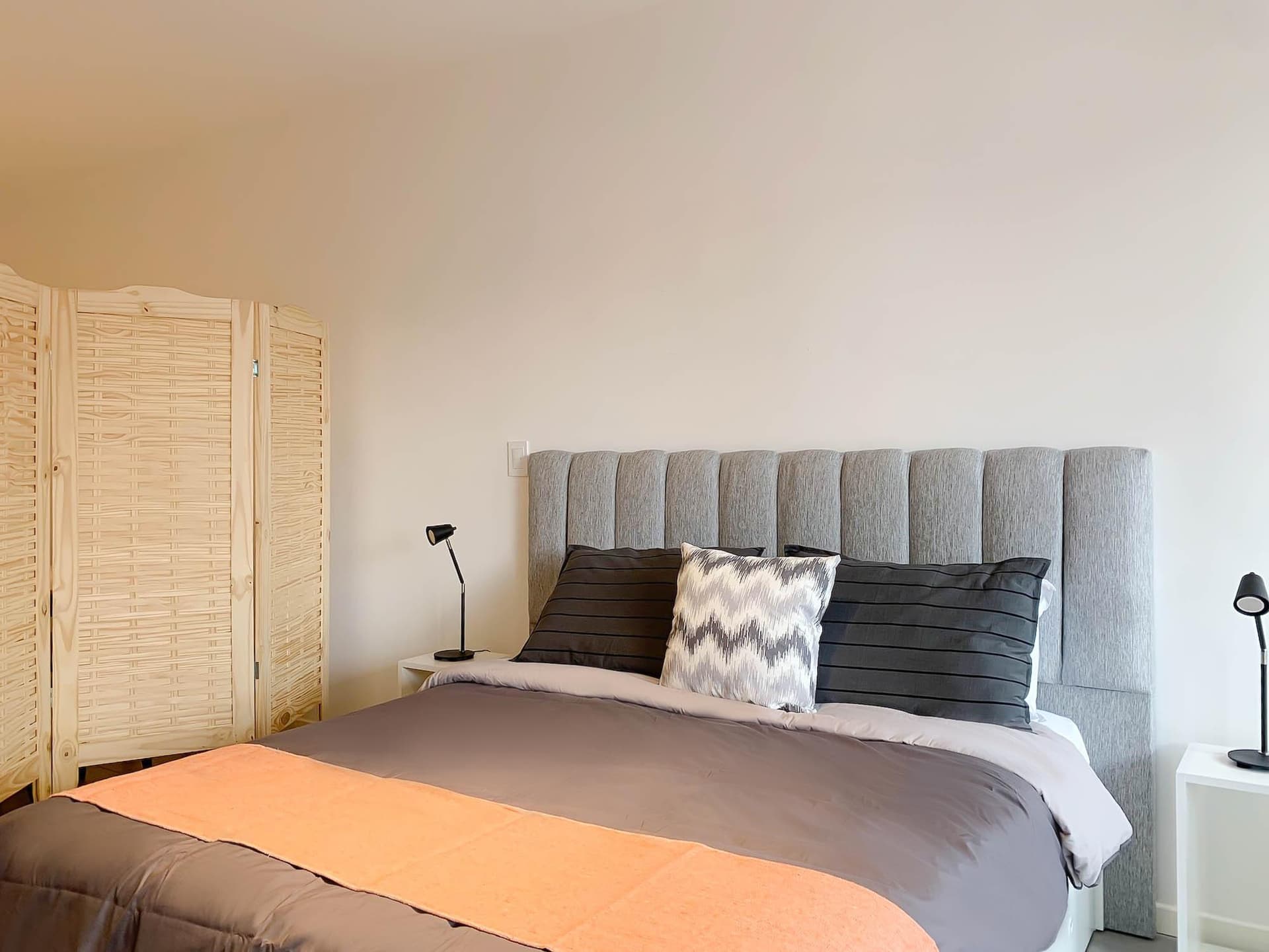 Dormitorio con cama, cabecera gris y biombo de madera.