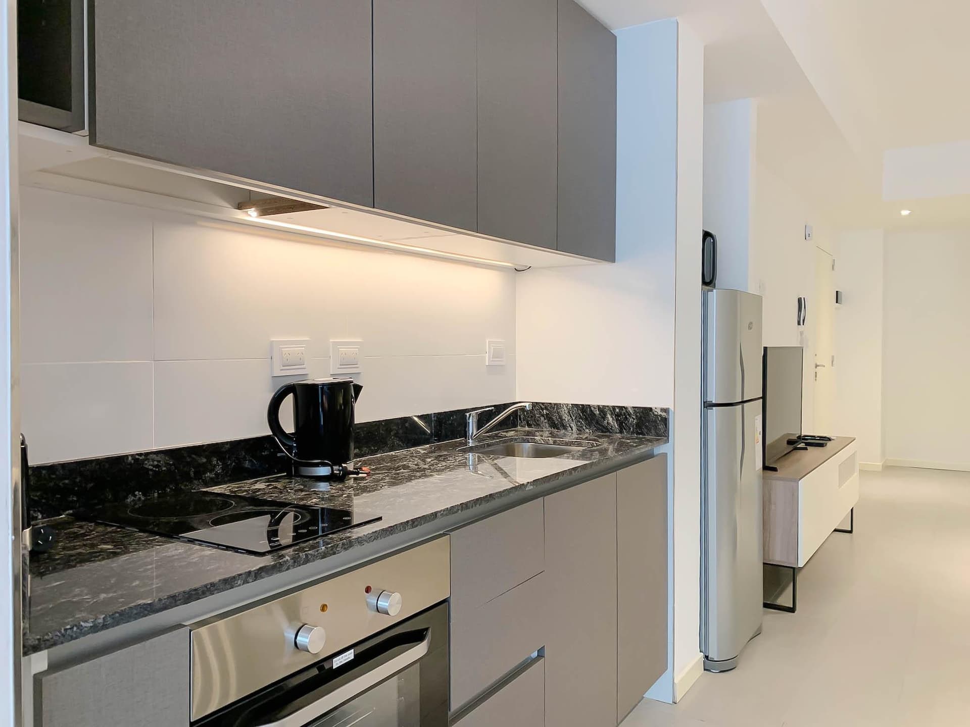 Cocina con mesada de granito, anafe, horno y alacenas grises.