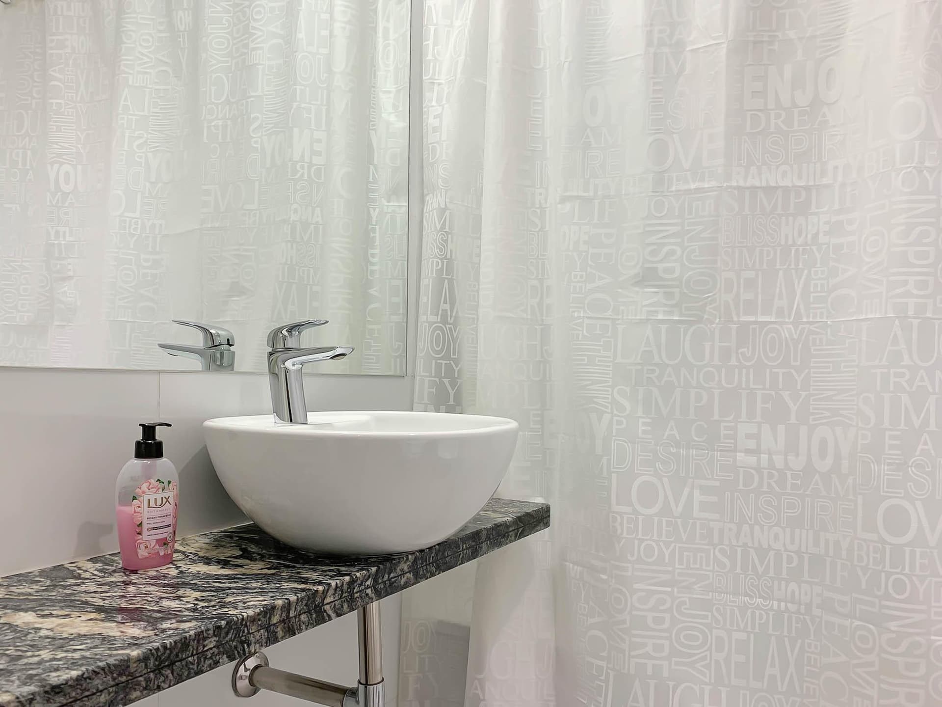 Baño con lavatorio de bacha, grifería cromada y cortina de ducha.
