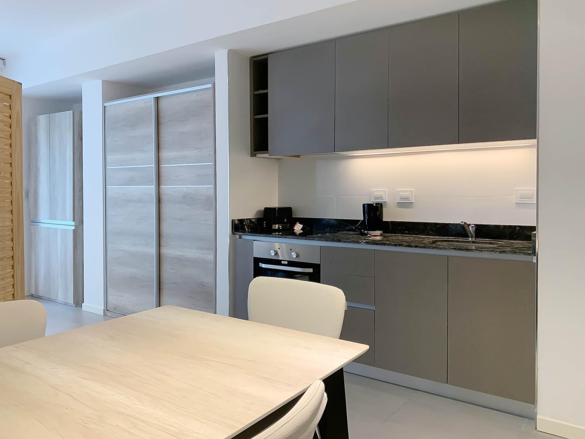 Cocina integrada con mesada, horno y alacenas grises.