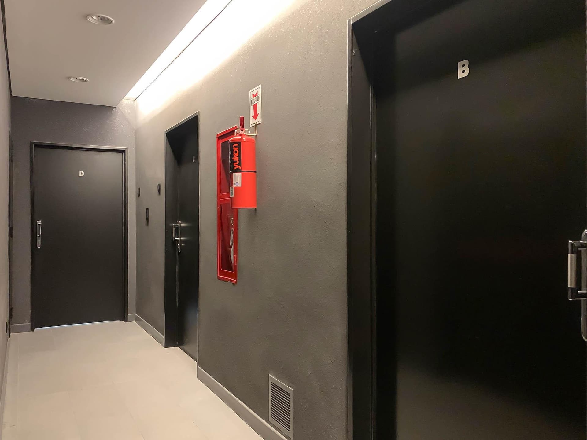 Pasillo de entrada del edificio con puertas y extintor.