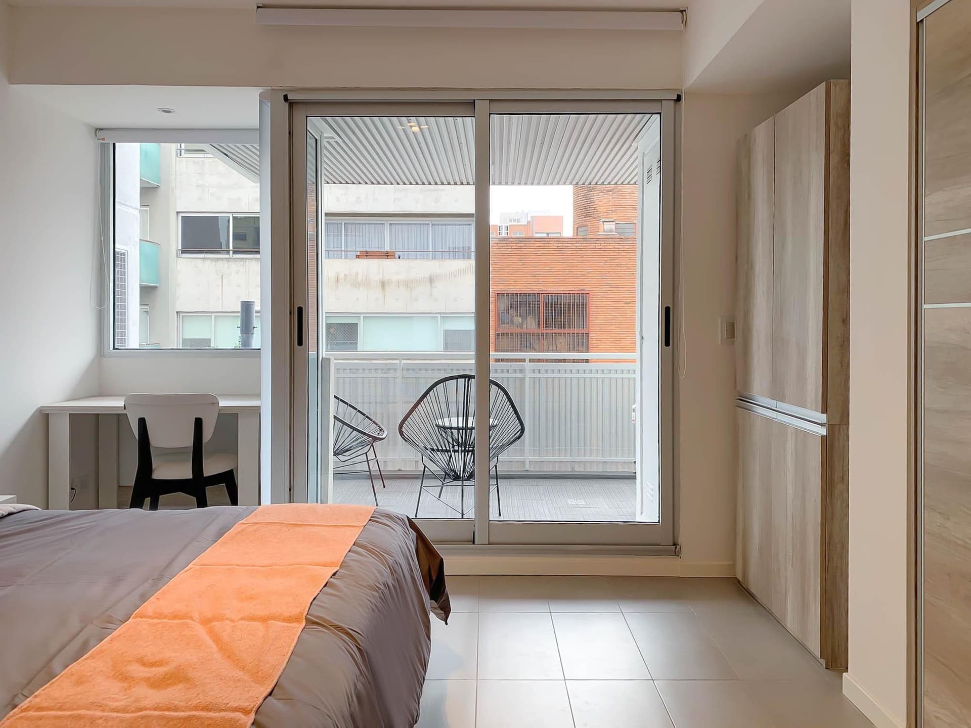 Dormitorio con cama hecha, escritorio, balcón y placard.