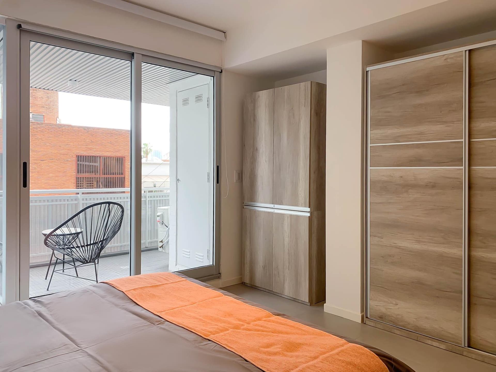 Dormitorio con cama, balcón, y placard de madera con puertas corredizas.