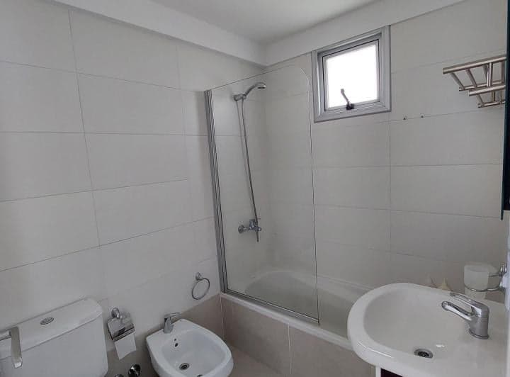 Baño con inodoro, bidet, bañera con mampara de vidrio y ventana.