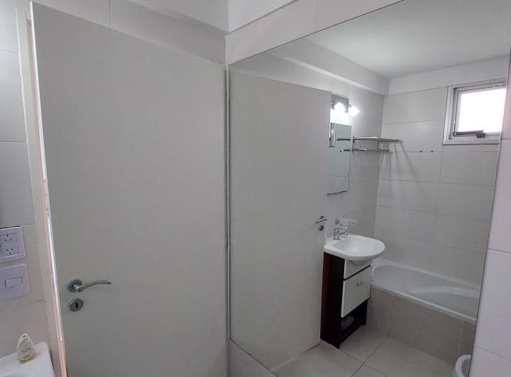 Baño con lavatorio, bañera y espejo grande, puerta abierta.