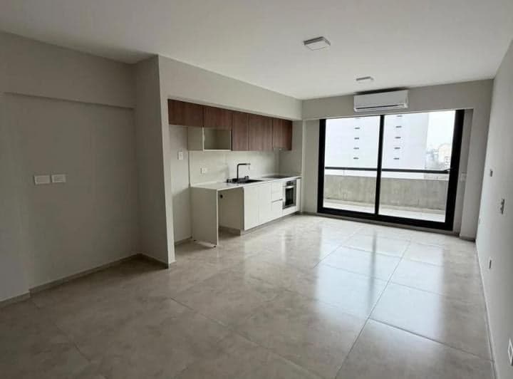 Ambiente principal vacío con cocina integrada, ventanal y piso de baldosas.