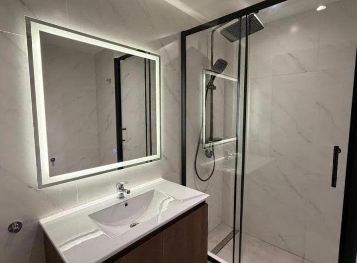 Baño moderno con vanitory, espejo iluminado y cabina de ducha.