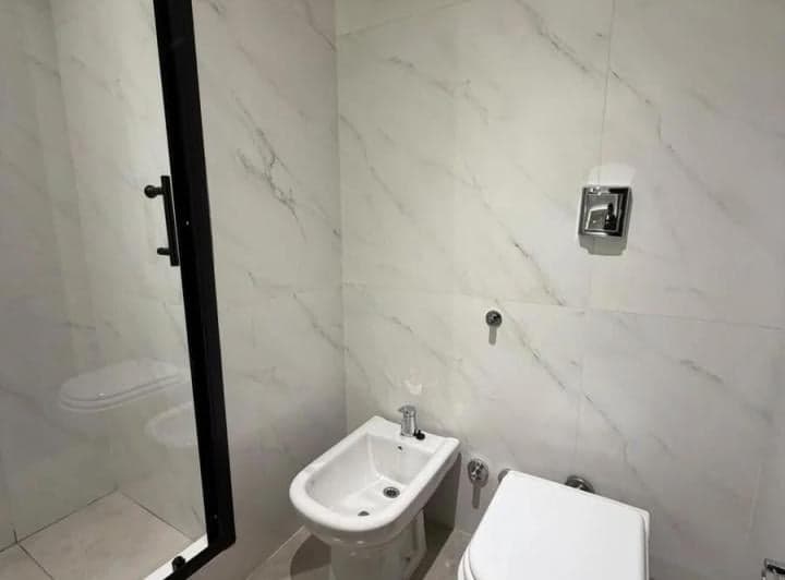 Baño con azulejos blancos, inodoro y bidet, y parte de la ducha.