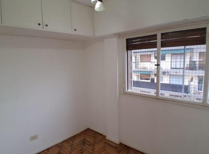 Dormitorio vacío con ventana, placard aéreo y piso de parquet.