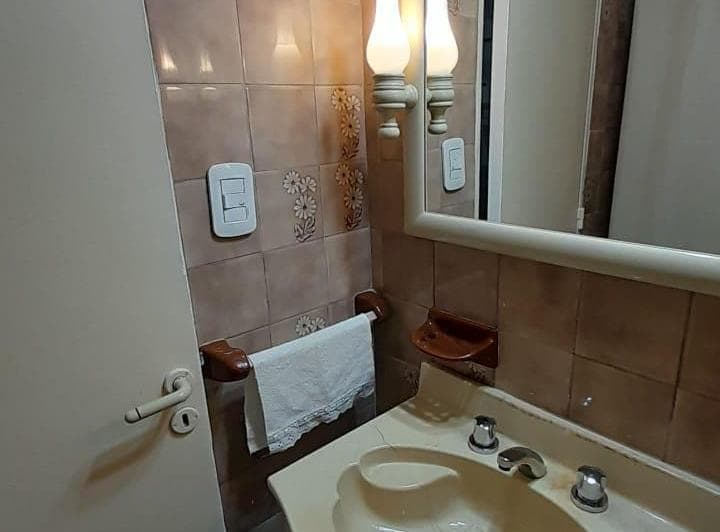 Baño con lavatorio, espejo y azulejos marrones con diseño floral.