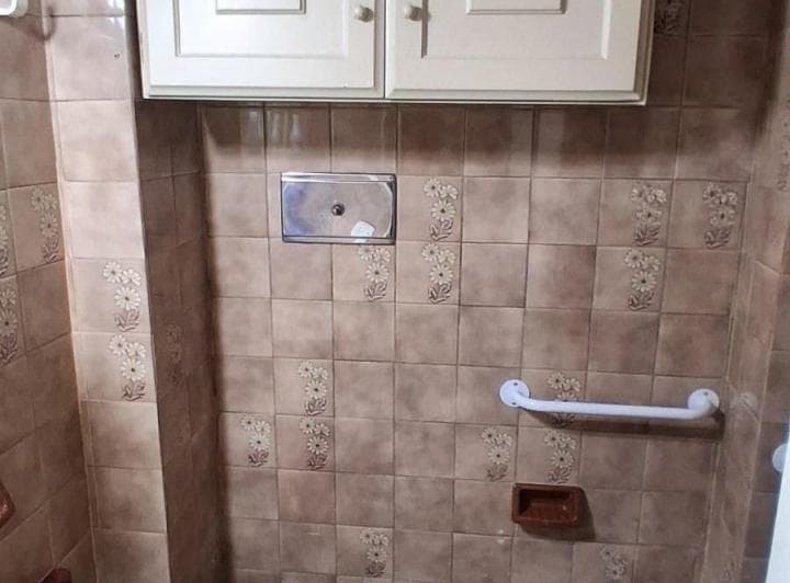 Baño con inodoro, azulejos marrones con diseño floral y estantes.
