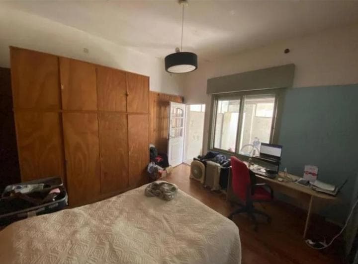 Dormitorio con cama, placard de madera y escritorio con computadora.