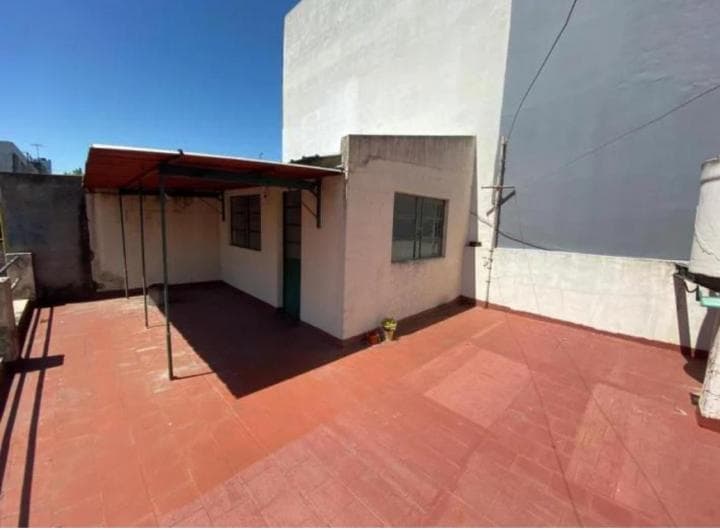 Terraza amplia con piso cerámico rojo y construcción pequeña.