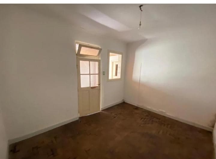 Dormitorio vacío con piso de madera, paredes blancas y puerta.
