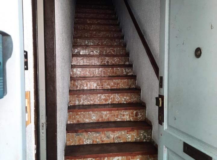 Pasillo de entrada con escalera, peldaños de azulejos y baranda.