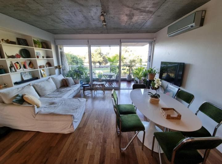 Living-comedor con sillón blanco, mesa de comedor y estantería, vista al balcón.