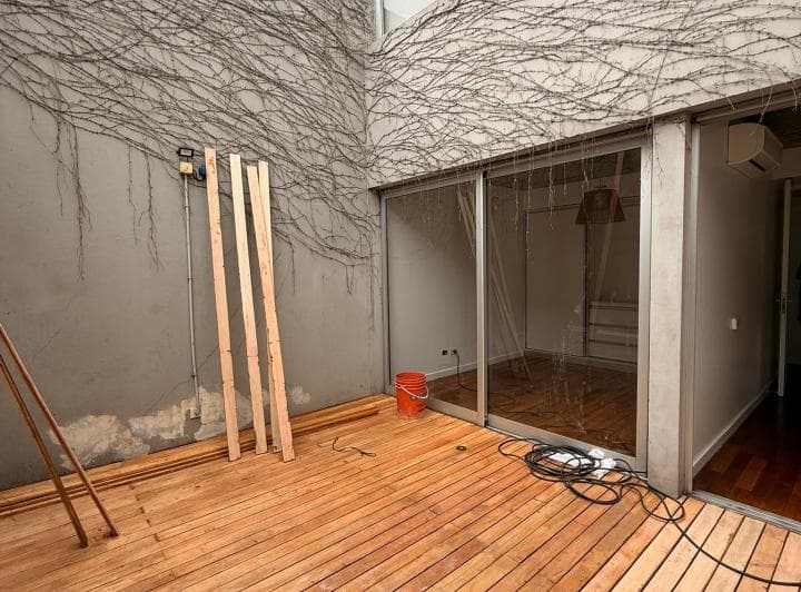 Patio de madera con enredadera en la pared y salida a un cuarto.