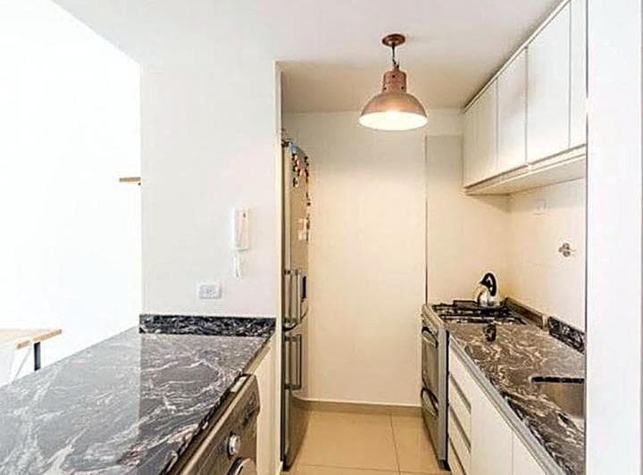 Cocina con heladera, mesada de granito, alacenas blancas y hornalla.