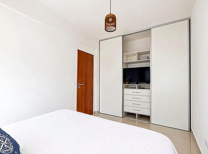 Dormitorio con cama matrimonial, placard blanco empotrado y puerta de madera.