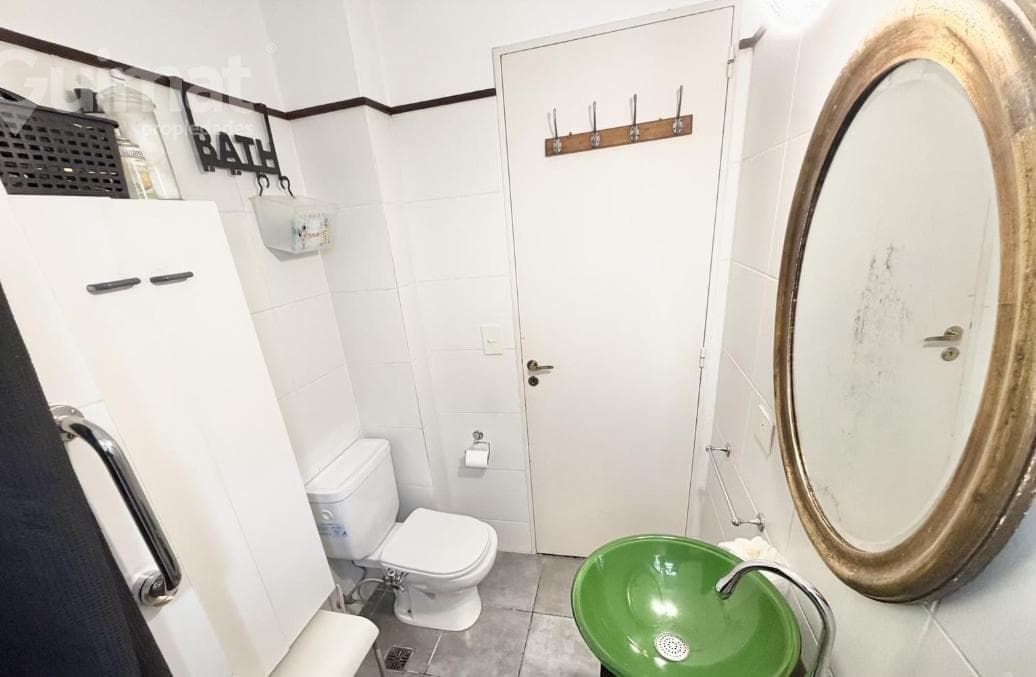 Baño con inodoro, vanitory con bacha verde, espejo ovalado y ducha.
