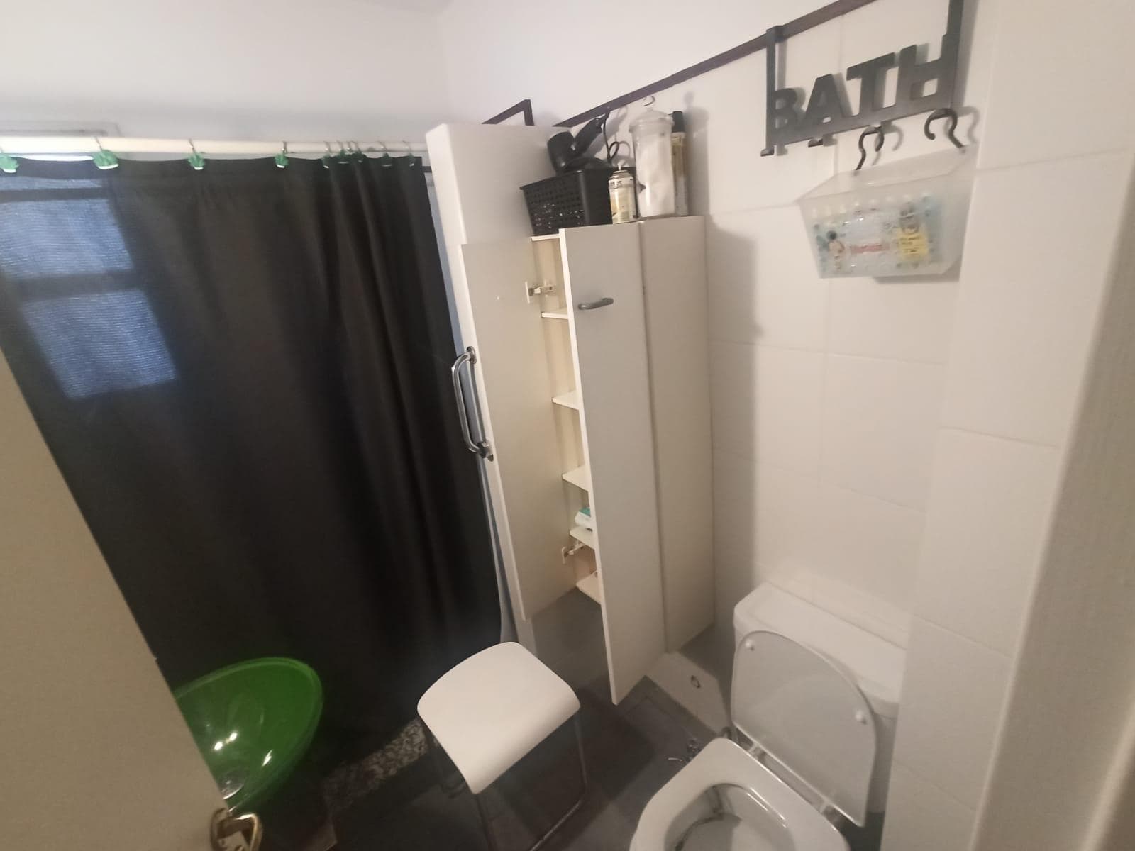 Baño con ducha con cortina, inodoro y mueble de guardado.