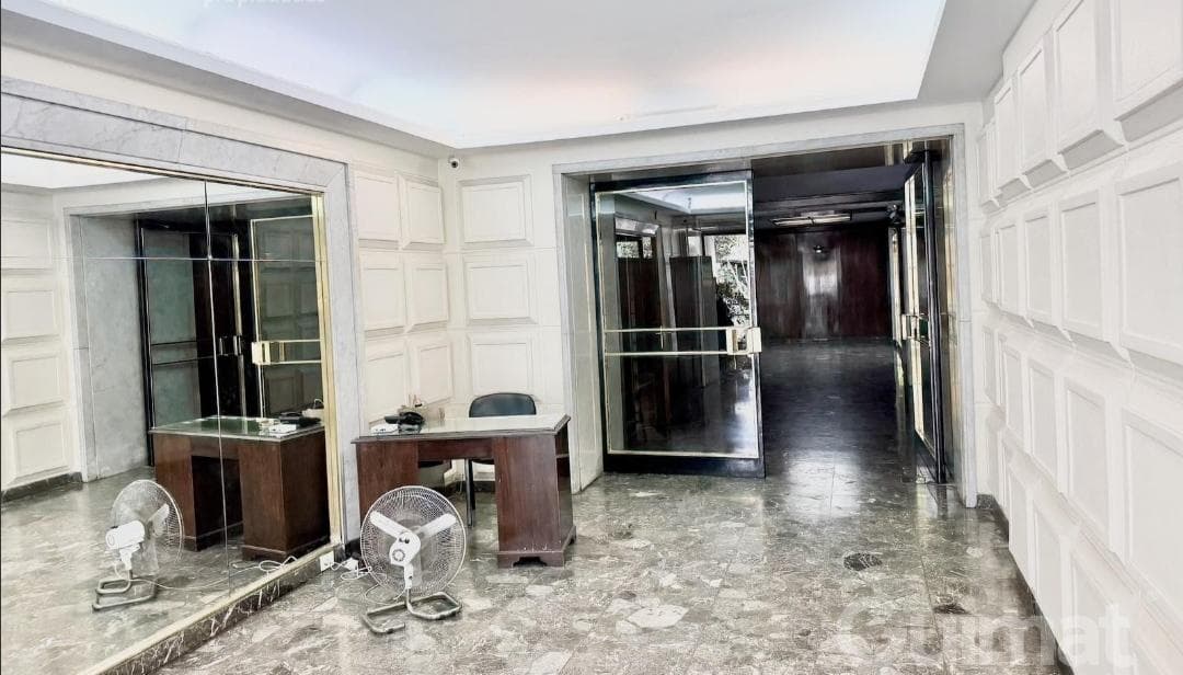 Hall de entrada del edificio con espejos, escritorios y acceso a ascensores.