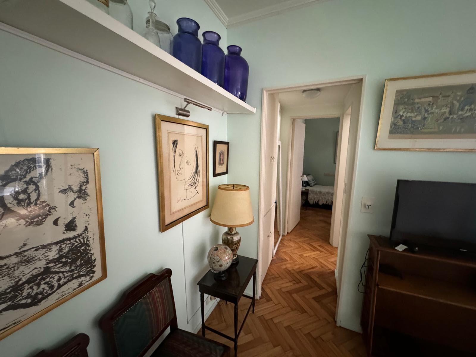 Pasillo de distribución con cuadros, lámpara y piso de parquet.