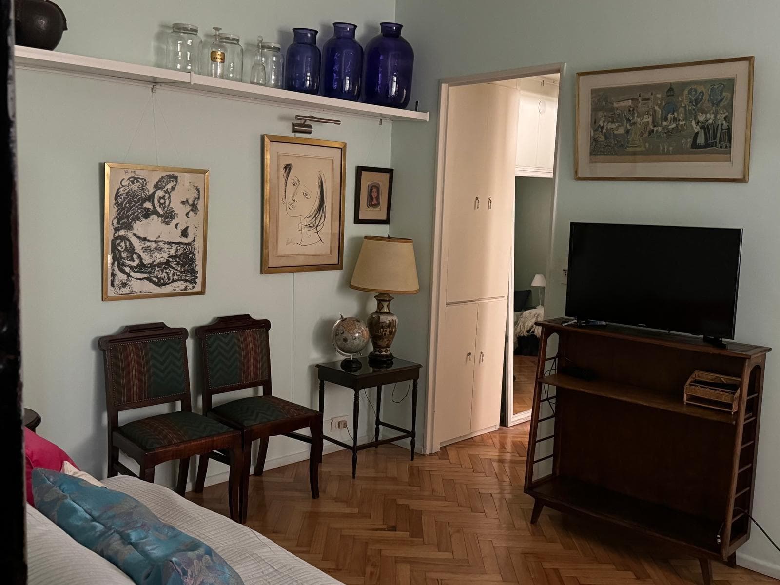 Living con sillón, televisión, estantes decorativos y acceso a otro ambiente.