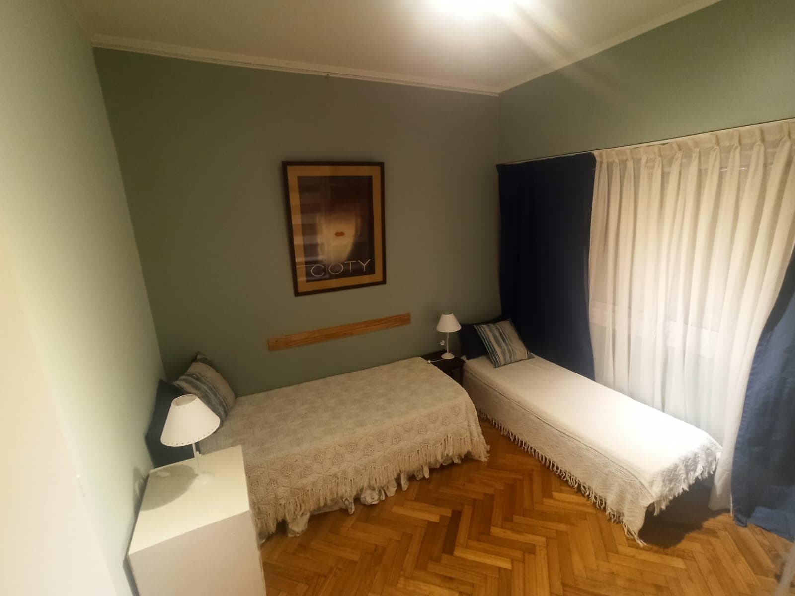 Dormitorio con dos camas individuales, mesas de luz y ventana con cortinas.