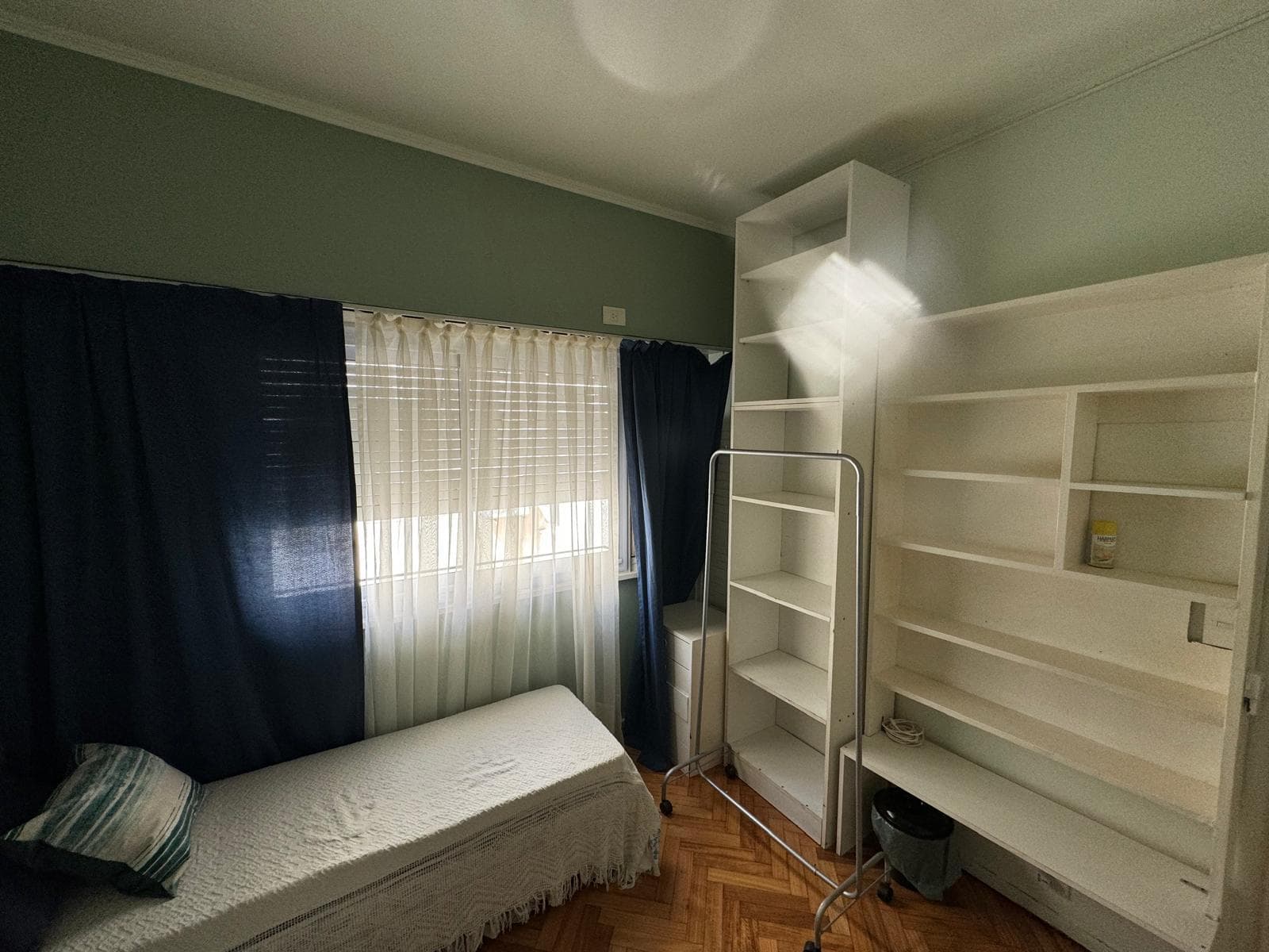 Dormitorio con cama individual, estanterías y ventana con cortinas.