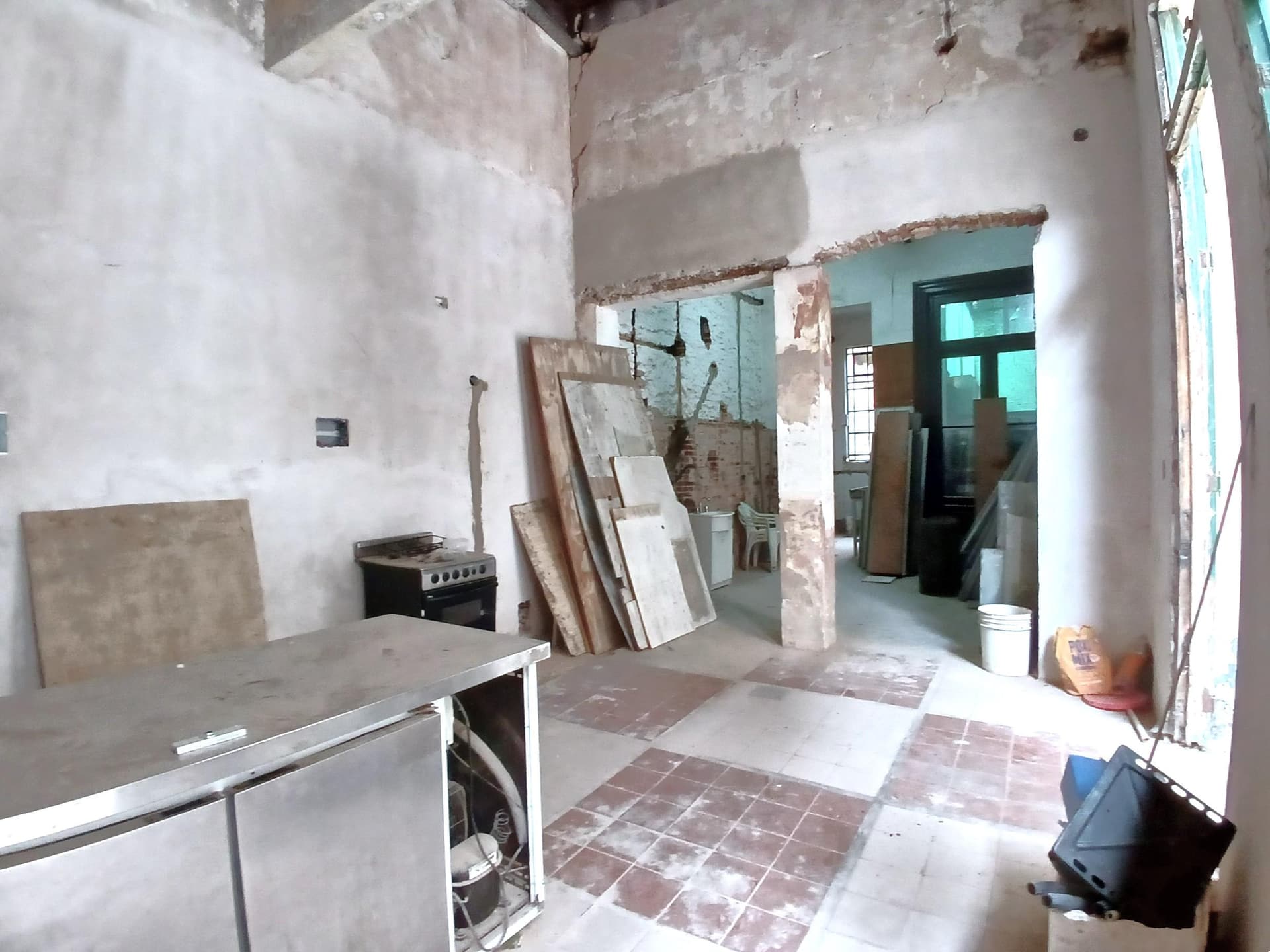 Cocina con mesada de acero, horno, alacenas y paredes en refacción.