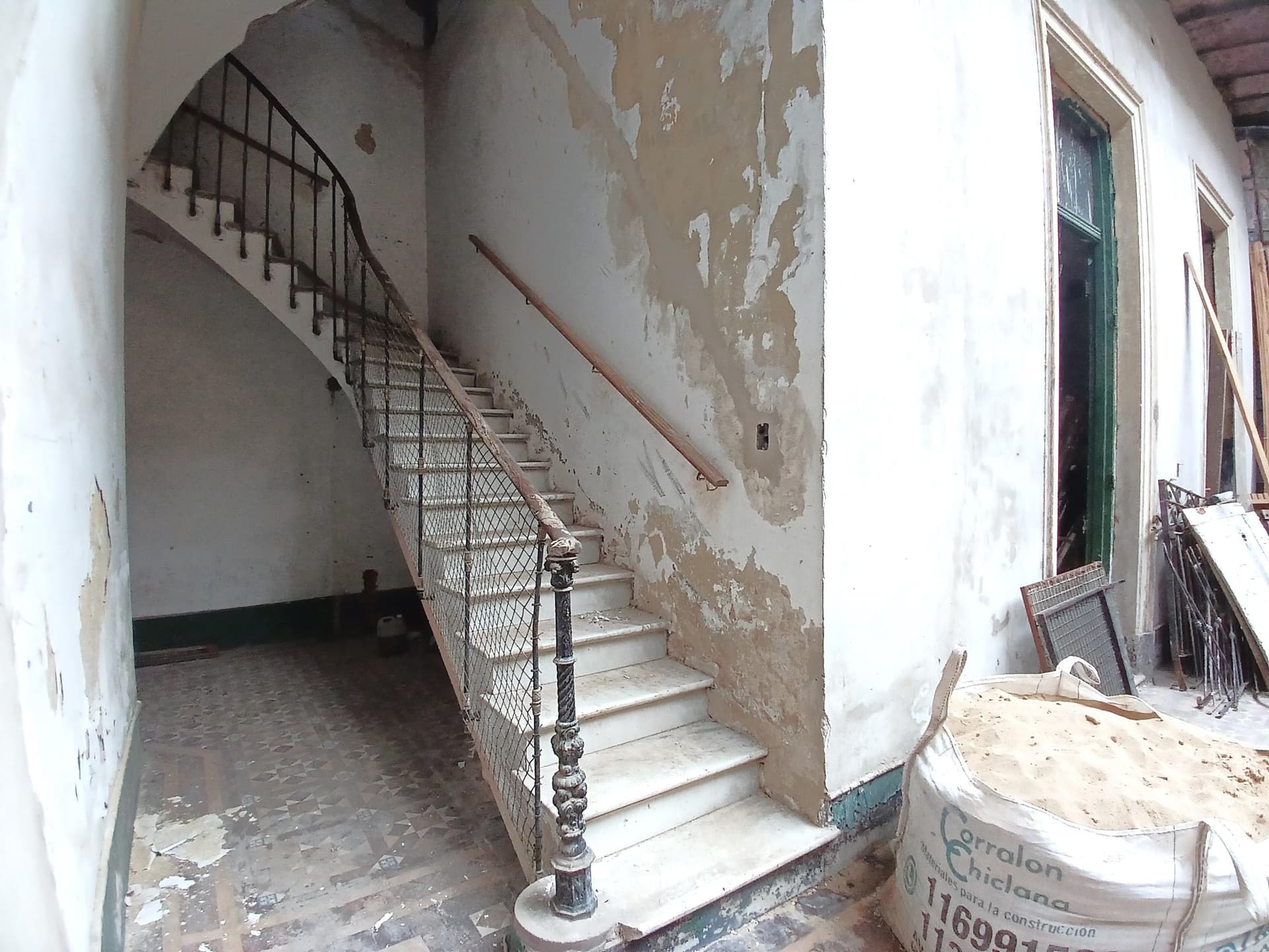 Escalera de mármol con baranda de hierro forjado y paredes descascaradas.