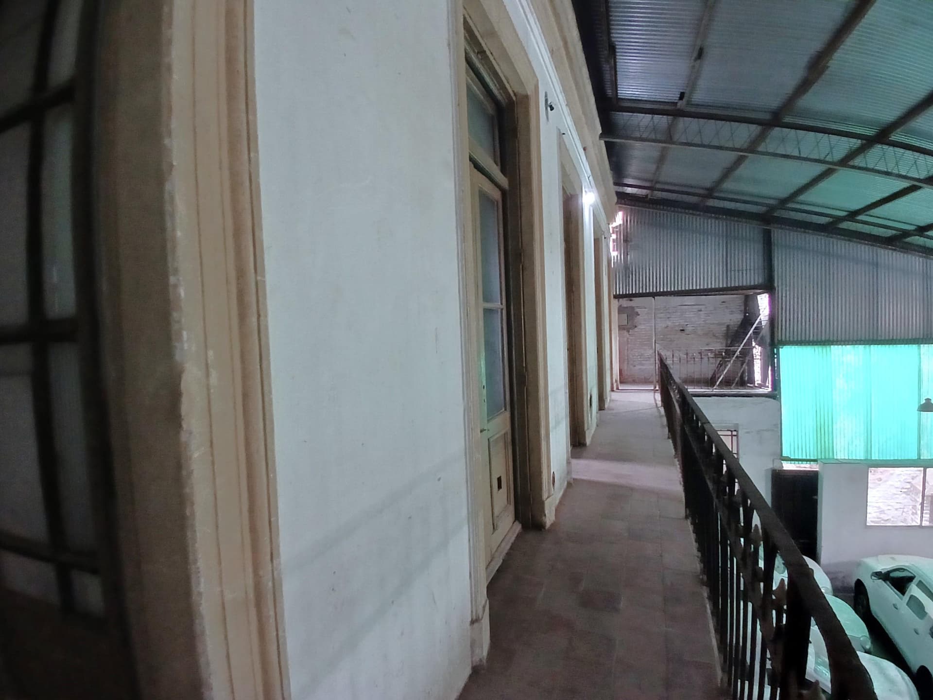 Pasillo exterior en planta alta con baranda de hierro y techo de chapa.